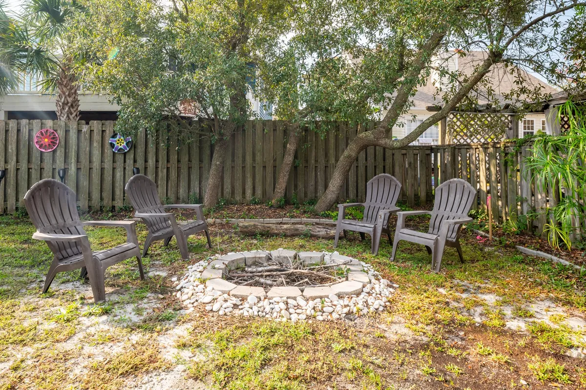 A cozy fire pit surrounded by Adirondack chairs, set against a backdrop of trees and a sturdy fence. The space is designed for evening gatherings, storytelling, and stargazing under the open sky.