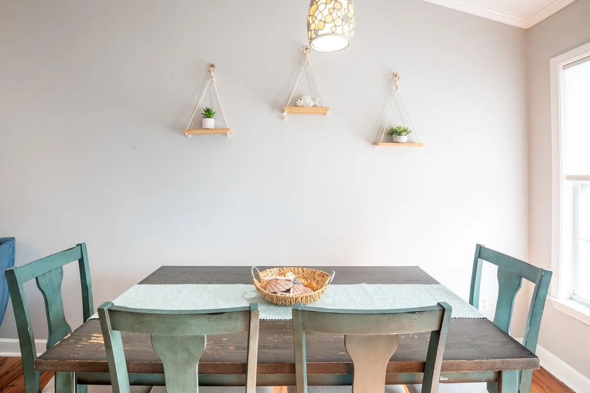 A welcoming dining space centered around a large wooden dining table, illuminated by a stylish light fixture above. Hanging shelves and decor add warmth to the room, creating a perfect setting for family meals, board games, or planning adventures together.