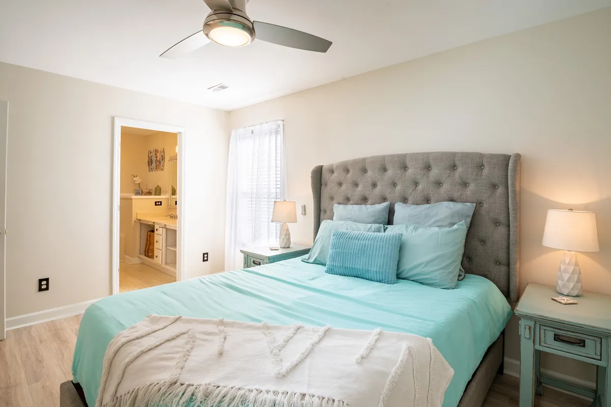 A tranquil bedroom featuring a king-size bed with a tufted headboard, soft blue bedding, decorative pillows, and matching bedside tables. Soft morning light fills the space, creating a soothing and restful atmosphere ideal for a primary suite.