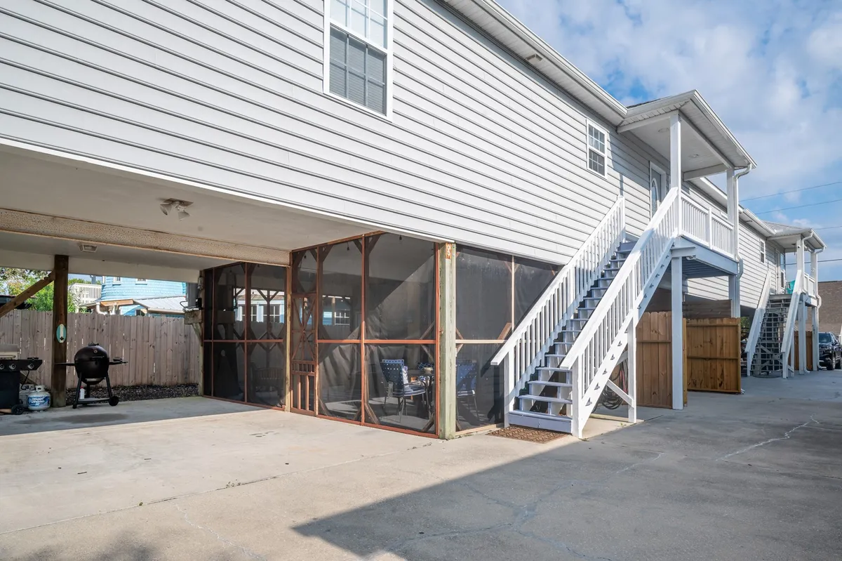 A screened-in porch with comfortable outdoor seating, stairs leading down to the yard, and a grill ready for barbecuing. String lights add a festive touch, and the space is both welcoming and practical for gatherings.