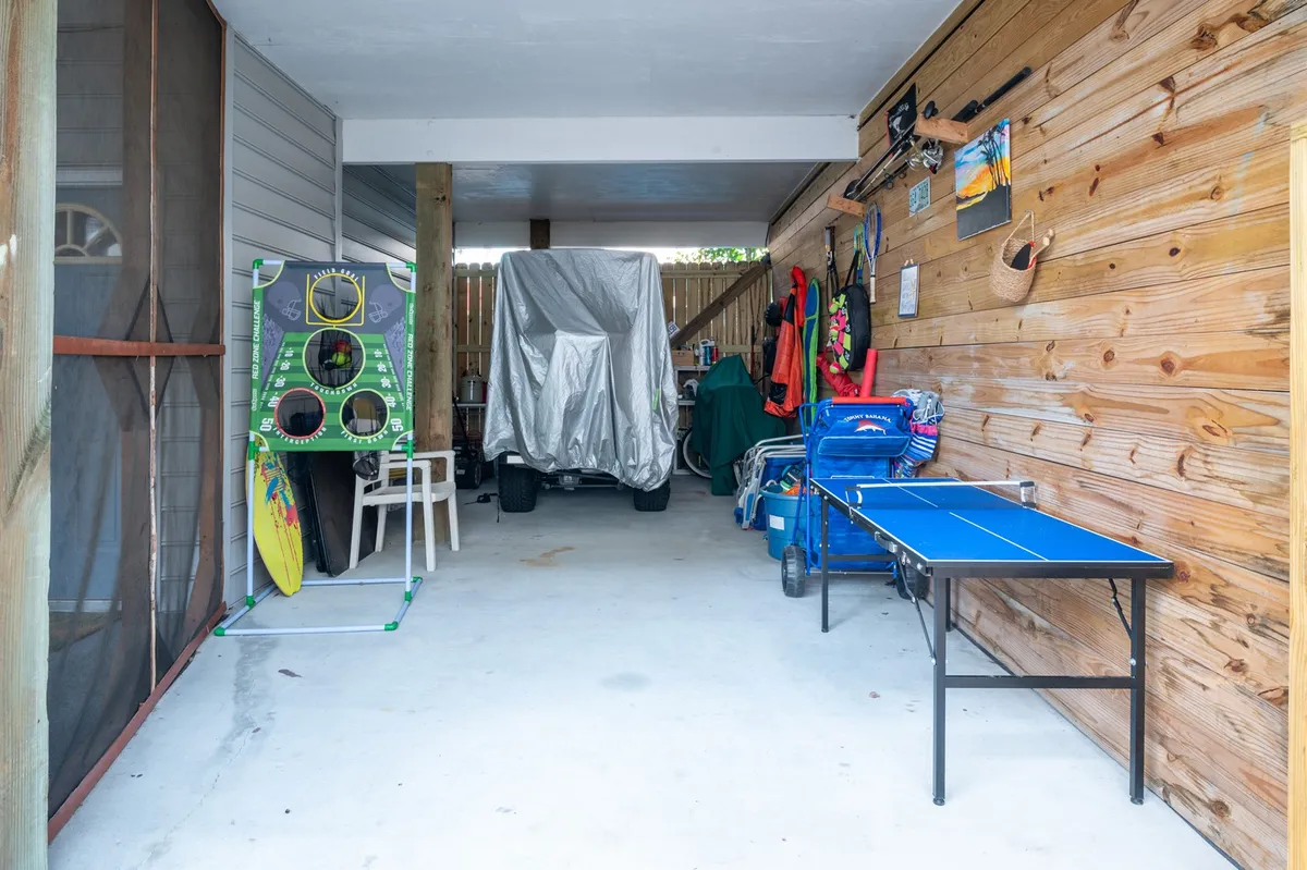 A lively rec room featuring a ping pong table and sports equipment, with colorful storage bins and a covered vehicle in the background. The space is casual and designed for active fun and easy access to outdoor gear.