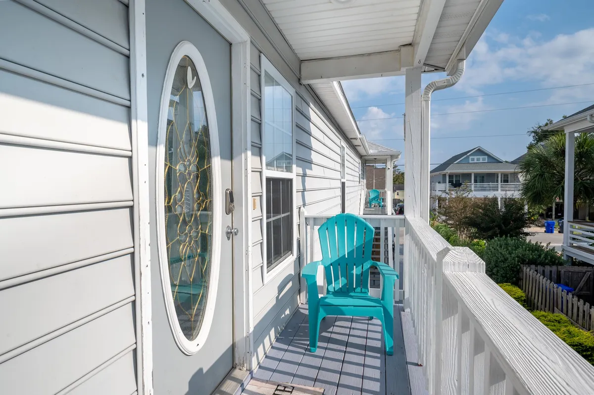 A welcoming exterior shot featuring a turquoise chair by a decorative door and a window with reflective glass. The scene captures the essence of coastal relaxation, encouraging moments of unwinding after a day of boardwalk fun or watching sunsets from the porch.
