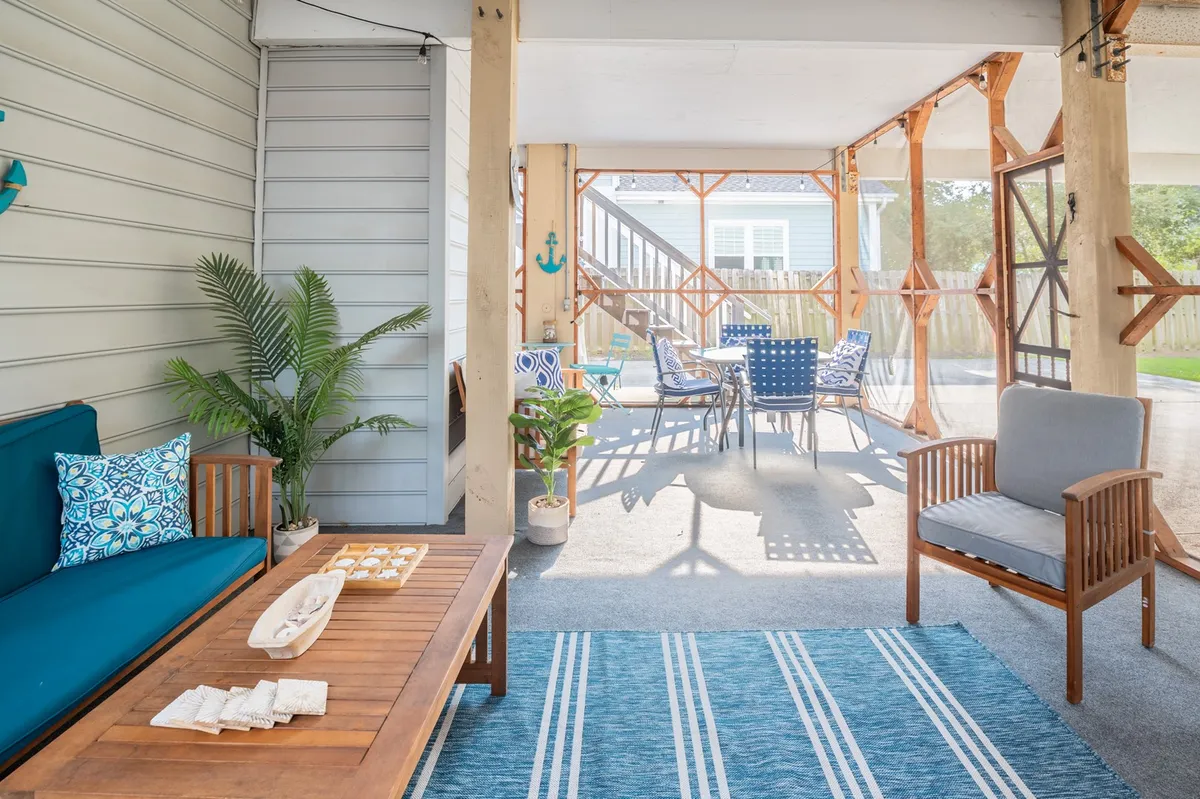 The image showcases a bright and inviting living space featuring a plush blue couch, a warm wooden coffee table, and a striped rug that adds a coastal touch. In the background, a spacious dining area with chairs suggests room for family meals or group celebrations, all bathed in natural light for a welcoming, airy feel.