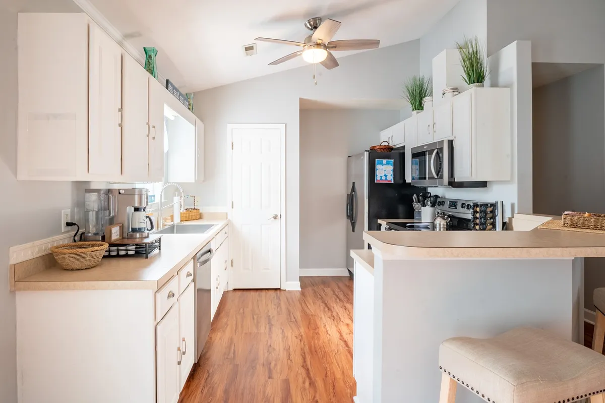 A bright, modern kitchen featuring a spacious countertop, sleek appliances, and a bar seating area. Natural light pours in from a large window, illuminating the space and highlighting the kitchen's inviting design. The arrangement is ideal for both meal prep and casual conversations, with room for multiple cooks or family members to gather.