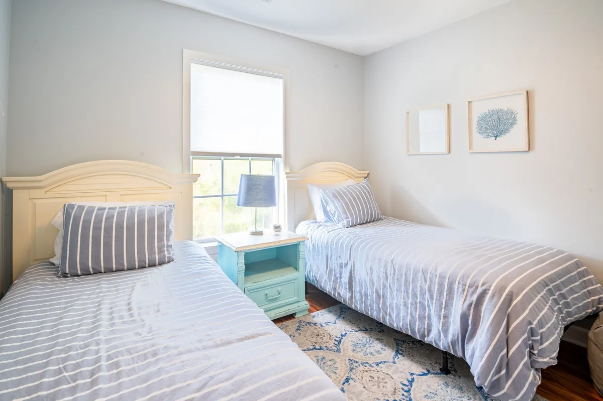 A cozy kids' or guest bedroom with two twin beds, a blue nightstand, and decorative wall art. The room has a peaceful feel, with soft lighting accentuating the intimate and family-friendly arrangement.