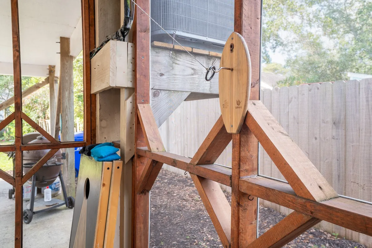 A cozy outdoor gathering space with a wooden pulley system, comfortable seating with colorful cushions, and a grill in the background. The scene evokes the warmth of shared meals and lively conversation, perfect for al fresco dining or a casual cookout.